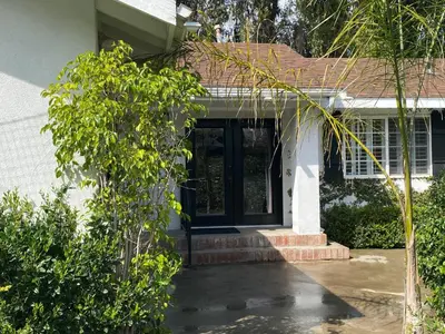 a white house with a black door and trees at Guest house with private entry and large pool in Los Angeles