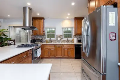 a kitchen with a stainless steel refrigerator and wooden cabinets at Central LA Bliss: 5 BR Home, BBQ, Perfect Location in Los Angeles