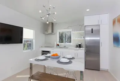 a white kitchen with a table and a refrigerator at Elegant Ocean View Studio in Prime Santa Monica Location in Los Angeles