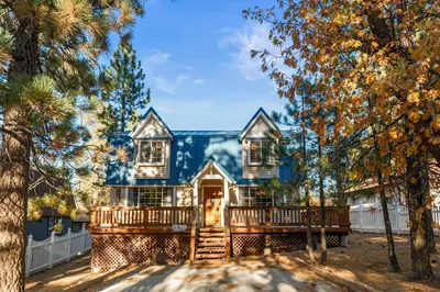 a blue house with a deck and trees at Hillcrest HappyNest - Hot tub, fire pit, gas grill in Big Bear Lake