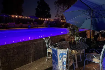 a table and chairs next to a pool at night at Rio Bravo Country Club Home in Bakersfield with Pool in Bakersfield