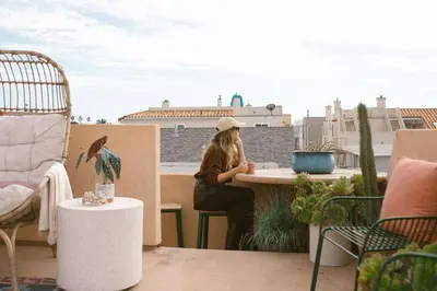 a woman sitting at a table on a balcony at Cool Cali Vibe - Barefoot Stepping Distance 2 Sand in Oxnard
