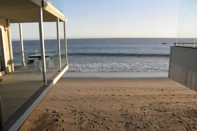 a beach with a building and the ocean in the background at Malibu Private Beach Apartments in Malibu