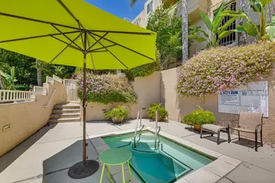 a green umbrella and a table and chair next to a pool at 2 Mi to Hollywood Condo with Pool and Hot Tub Access in Los Angeles