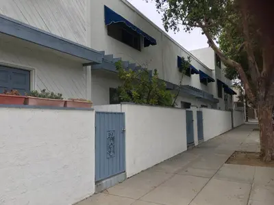 a white building with blue doors and a sidewalk at Coastal Comfort Homestay in Santa Monica in Los Angeles