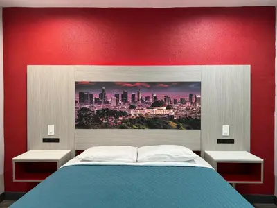 a bed with a red wall with a picture of a city at Playa Inn Motel - Long Beach, LA in Long Beach