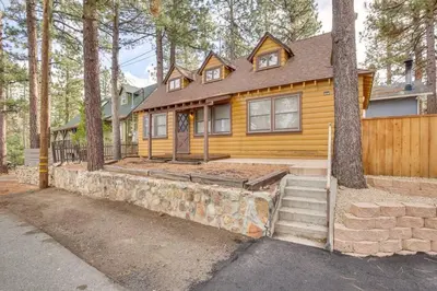 a yellow house with a stone wall and trees at The Twin Pines Chalet, 2 min to Village, BBQ in Big Bear Lake