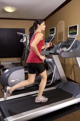 a woman running on a treadmill in a gym at Folk Inn Ontario Airport in Racimo