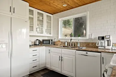 a white kitchen with white cabinets and a window at Quiet Mountain Cabin in Lake Arrowhead