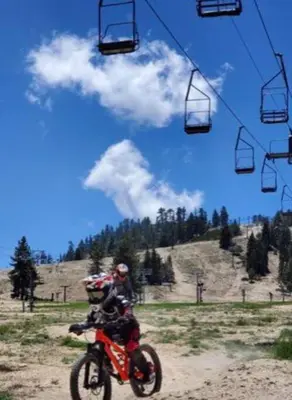 a person riding a motorcycle on a dirt road next to a ski lift at The Muddy Moose- Spacious Family Getaway in Lake Arrowhead