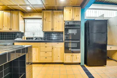 a kitchen with wooden cabinets and a black refrigerator at Walk to Abbot Kinney Tranquil Cottage in Venice! in Los Angeles