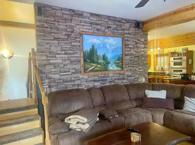 a living room with a brown couch against a stone wall at Cabin 7 sleeps 8 BEAUTIFUL BOULDER BAY, BIG BEAR in Big Bear Lake