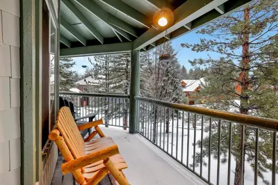 a wooden bench sitting on a porch with snow covered trees at Castle Glen Gem #2220 in Big Bear Lake