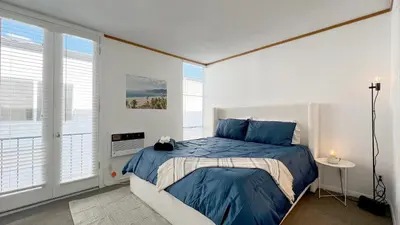 a bedroom with a bed with blue sheets and windows at Coastal Retreat Steps from the Santa Monica Beach in Los Angeles