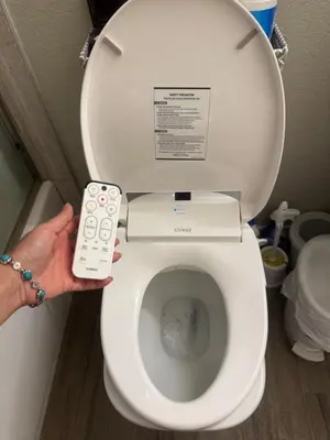 a person holding a remote control in front of a toilet at villa Double Room in Chino Hills