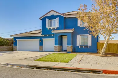 a blue house with two white garage doors at Pool Table and Charcoal Grill Home in Victorville! in Victorville