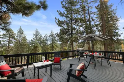 a deck with tables and chairs and an umbrella at Casita de Sergio - Peek-A-Boo Lake View, Walk to Lake, Fireplace in Big Bear Lake