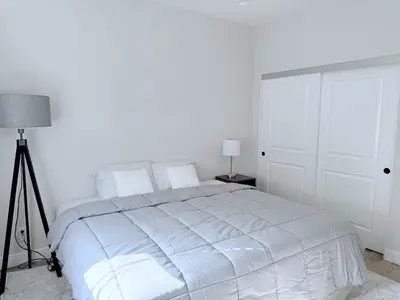 a white bedroom with a bed and a lamp at Modern Family Haven - Minutes from Disney Magic-OC in Midway City
