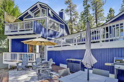 a blue house with a table and an umbrella at Serenity Cove Lake House by Big Bear Vacations in Big Bear Lake