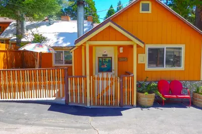 an orange house with two red chairs and an umbrella at Sleepy Hollow Cabins and Hotel in Crestline
