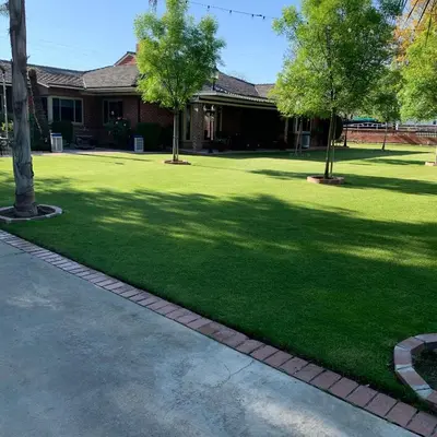 a yard with green grass and trees in front of a house at Cozy Room in Bakersfield