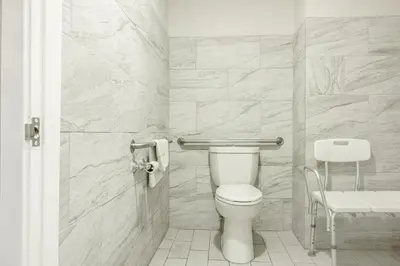 a white bathroom with a toilet and a chair at Hotel Avenida Victorville I 15 in Victorville