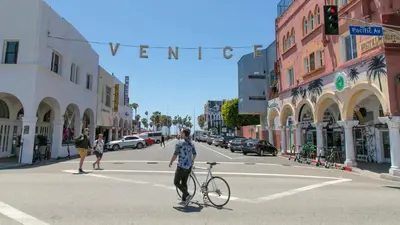 a man crossing a street with a bike in the street at Walk to Santa Monica Beach & Pier I Free Parking! in Los Angeles