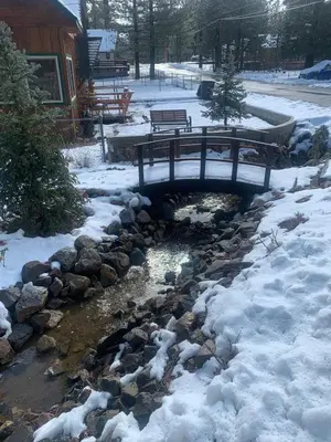 a bridge over a stream with snow on the ground at Spacious cozy chalet huge deck over seasonal creek in Big Bear City Airport