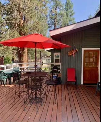 a deck with a table and chairs and an umbrella at Spacious cozy chalet huge deck over seasonal creek in Big Bear City Airport