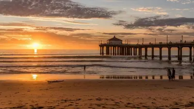 a pier on the beach with people standing in the ocean at 3BR Townhouse in Prime Manhattan Beach Location in Manhattan Beach