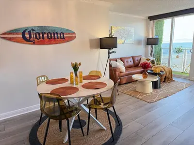 a living room with a table and a surfboard on the wall at Oceanfront 2 BR w Pool & Parking 234 in Hermosa Beach