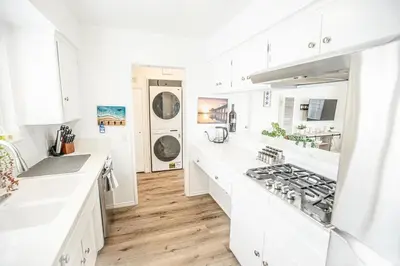 a white kitchen with wooden floors and white cabinets at Beach House Steps to the Sand! in Manhattan Beach