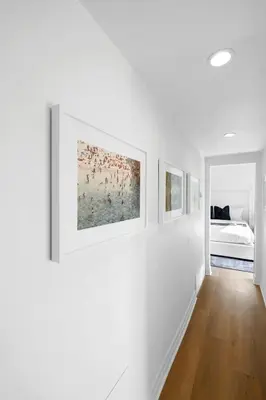 a white hallway with paintings on the walls at Malibu Beach House by Stay Awhile Villas in Malibu