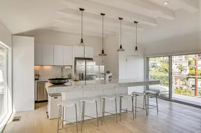 a kitchen with white cabinets and a large island with bar stools at Walk to Sunset Strip Modern Home in WeHo Hills! in Los Angeles