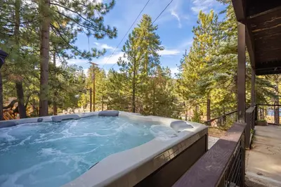 a hot tub on a deck with trees in the background at Ultimate Lakeview Lodge and ON THE LAKE! with a Hot-Tub! in Big Bear Lake