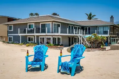 two blue chairs on the beach in front of a house at Carpinteria Dreamin by Paradise Retreats in Carpinteria