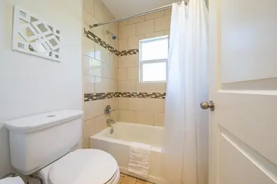 a white bathroom with a toilet and a tub and a window at F-56 Winnie the Poohs Treehouse in Anaheim