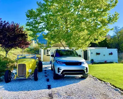 a car and a yellow cart parked in a driveway at Cozy Container in Devore Heights, California, for Glamping Getaways on Route 66 in Devore Heights