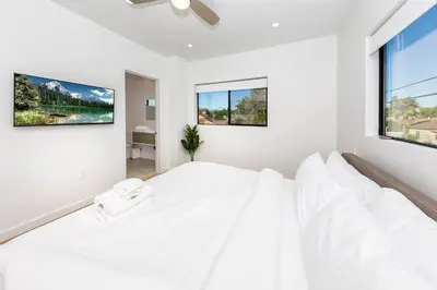 a white bedroom with a large bed and two windows at Modern 2BR Back House w/ TVs & Full Kitchen in Los Angeles