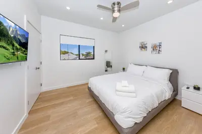 a white bedroom with a large bed and a tv at Modern 2BR Back House w/ TVs & Full Kitchen in Los Angeles