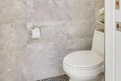 a bathroom with a white toilet and a tile wall at Private Pool and Sauna Pet-Friendly Reseda Retreat! in Reseda