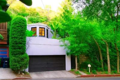 a white house with a garage and trees at Enchanting Hollywood Hills Oasis with Tree-Top Views, Serene Outdoor Living Room, Zen Garden, Free Attached Garage, Sleeps 6, in LA's Most Desirable, Central, Serene Canyon Neighborhood, and Only 2 Minutes to Hollywood Boulevard in Los Angeles