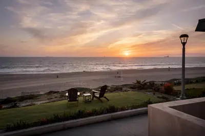 a sunset at the beach with two chairs and a table at New The Triton Manhattan Beachfront Escape in Manhattan Beach
