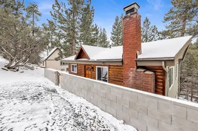 a log cabin in the snow with a brick chimney at Sueños Azules- Fawnskin Retreat Cottage in Big Bear in Fawnskin