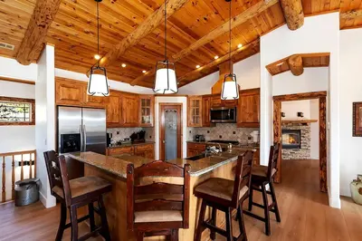 a kitchen with wooden cabinets and a large island with bar chairs at California Dreaming: Lakeside Cabin Getaway in the Best Location in San Bernardino