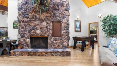 a stone fireplace in a living room with a table at The Fairway Hideaway by AvantStay Game Room Outdoor Dining Near Lake Arrowhead in Lake Arrowhead