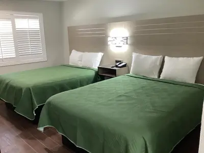two beds in a hotel room with green sheets at Mayfair Inn Onratio Airport & Convention Center in Ontario