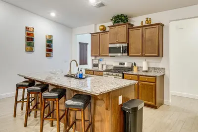 a kitchen with wooden cabinets and a large island with bar stools at 9 Mi to Dtwn Bakersfield Pet-Friendly Home in Bakersfield