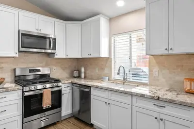 a kitchen with white cabinets and a stove and a sink at Modern Southwest Escape 2 Master Bedrooms in Bakersfield