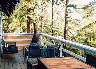 a deck with chairs and a table and a bottle of wine at Little Wolf Lodge Modern Cabin at Lake Gregory in Crestline